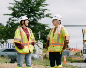 Woman on jobsite talking and laughing wearing hard hats and safety vest