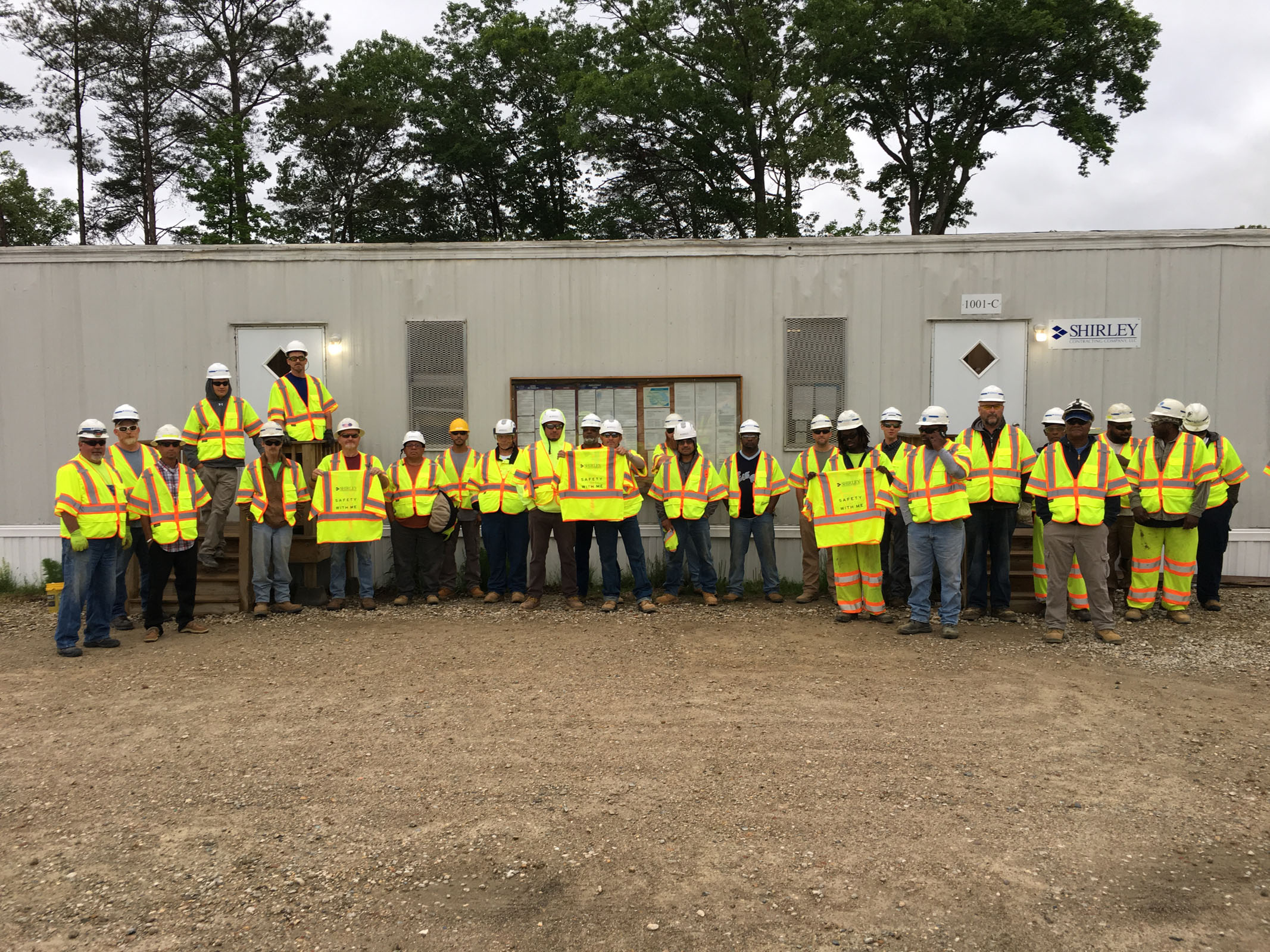 Workers in yellow protective vest posing for photo in front of trailer